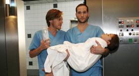 Klinik am Alex - Christian (Tobias Kay, l.) und Jens (Lee Rychter, r.) lassen sich in letzter Minute auf die risikoreiche Operation der kleinen Nina (India Fahey, liegend) ein. © Mosch Sat.1