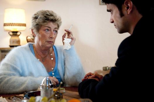Als Rita Kowalskis (Brigitte Janner, l.) Mann erschossen wird, stehen Mick und Andreas (Maximilian Grill, l.) vor einem Rätsel: Warum sollte jemand einem arbeitslosen Arbeiter vor laufendem Fernseher mitten ins Herz schießen? © SAT.1
